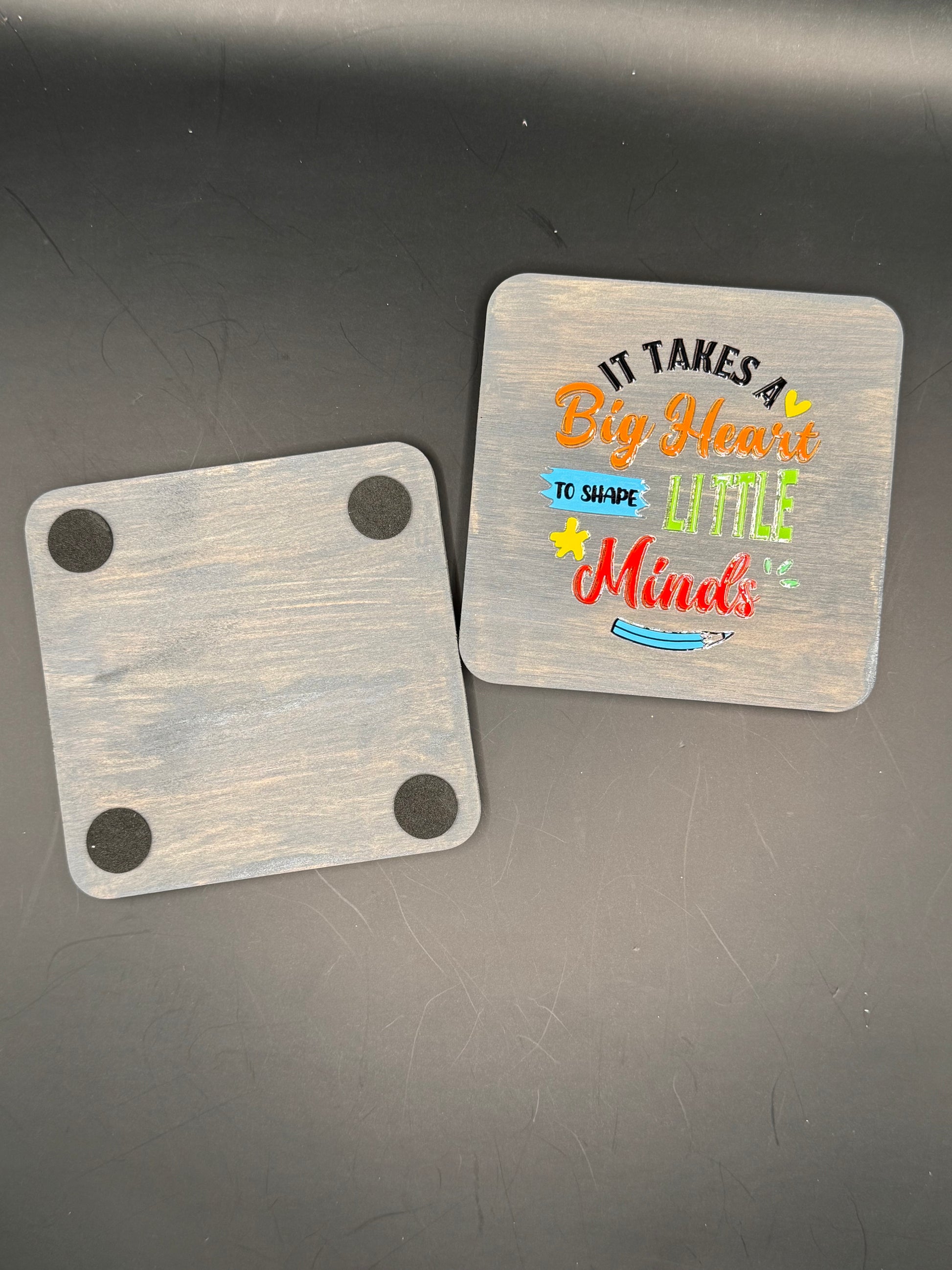 Two wooden coasters with text and designs on a dark surface